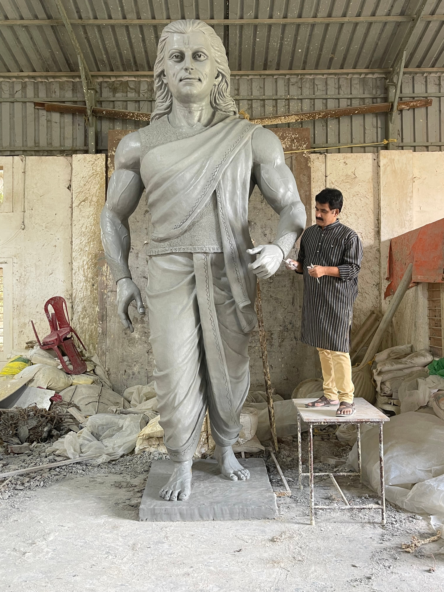 Over life-size warrior-saint figure in progress, sculpted by Dilip Rohom — shown alongside the artist for scale