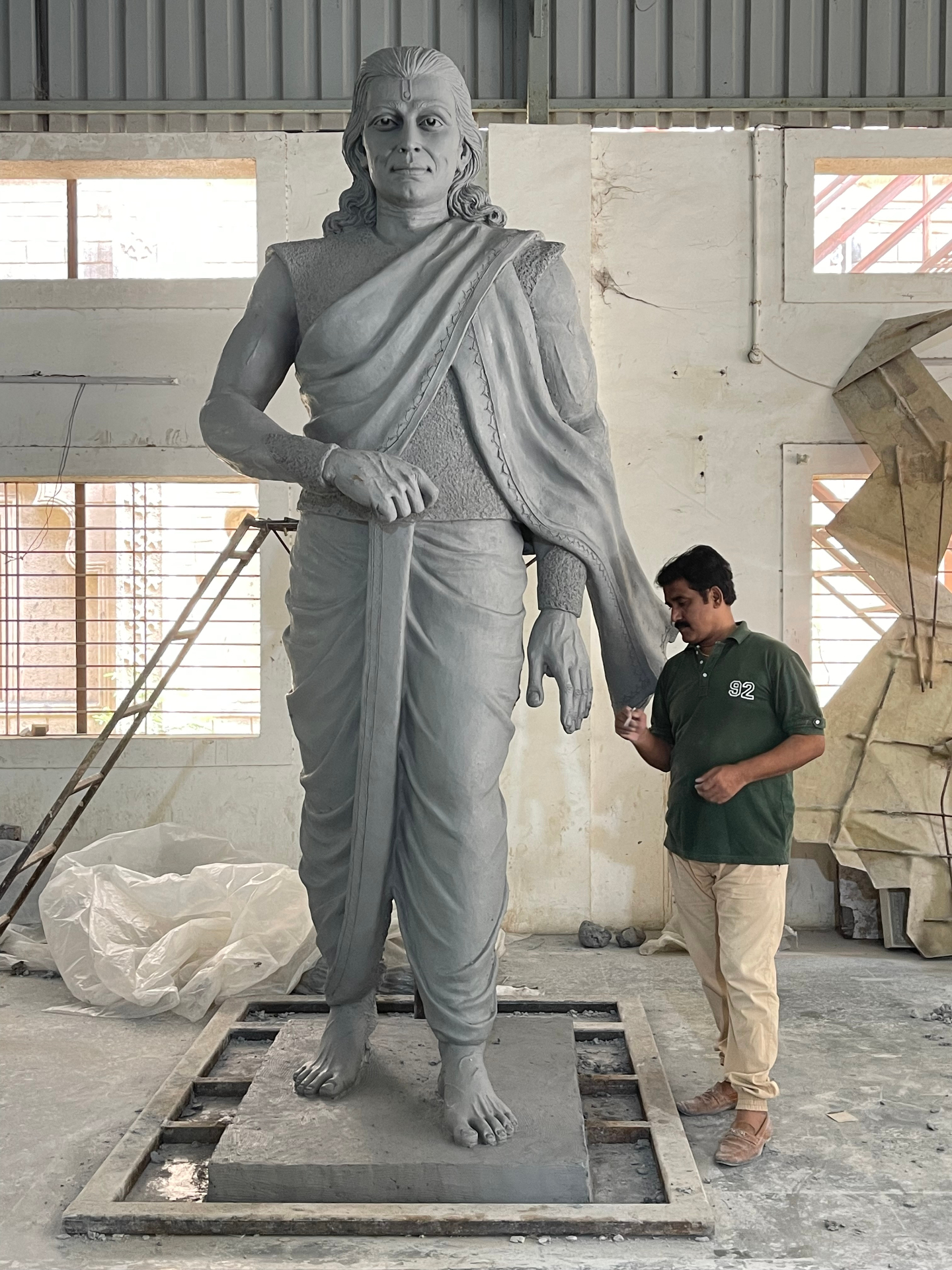Monumental clay figure in classical Indian attire, sculpted by Dilip Rohom — shown alongside the artist for scale